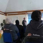 Two women in Autism Independence jumpers are part of the group watching Aga make her presentation